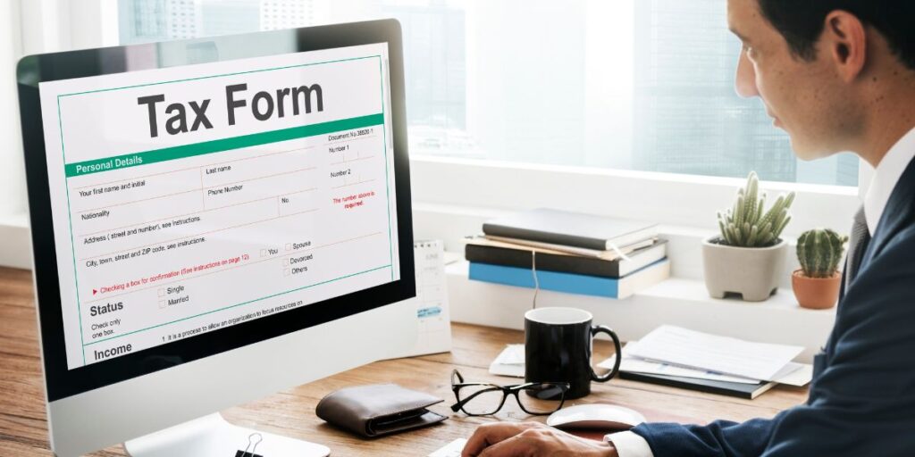 A businessman in a suit looks at a digital tax form on a computer screen in a modern office with a city view.